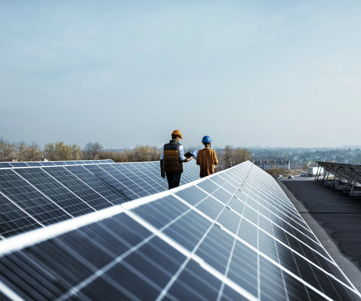 Blick auf das Dach einer grossen Überbauung. Zwei Experten begutachten die Solarpanels. Die Liegenschaft ist nach dem Prinzip Zusammenschluss zum Eigenverbrauch (ZEV) organisiert.