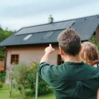Ein Vater hält sein Kind auf dem Arm und zeigt ihm die Solarpanels auf ihrem Hausdach. Dabei handelt es sich um eine Eigenverbrauchsvariante