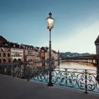 Im Hintergrund ist die Kapellbrücke in Luzern abends in der Dämmerung sichtbar, im Vordergrund steht eine Aussenbeleuchtung in Form einer Strassenlaterne